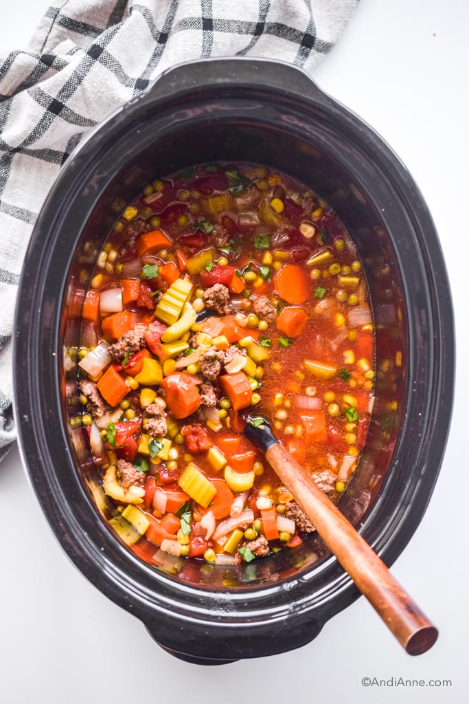 healthy hamburger soup in a slow cooker with kitchen towel beside it. Soup ladle with wooden spoon inside the slow cooker. 