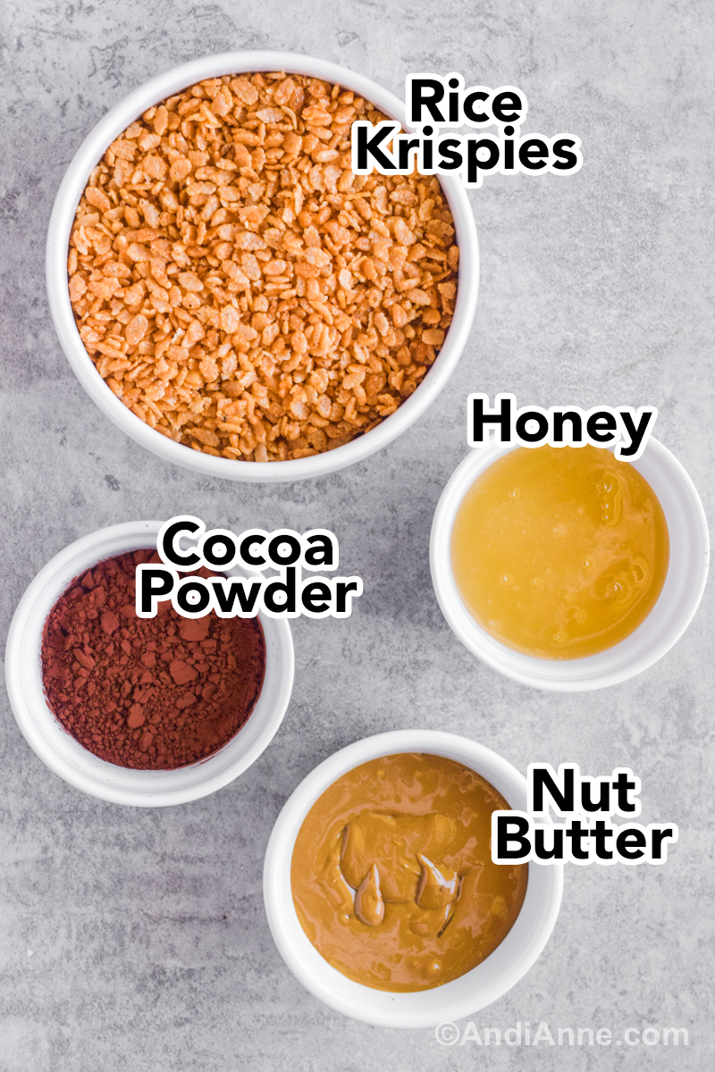 Recipe ingredients on a table. A bowl of rice krispies, bowl of honey, bowl of cocoa powder and nut butter.