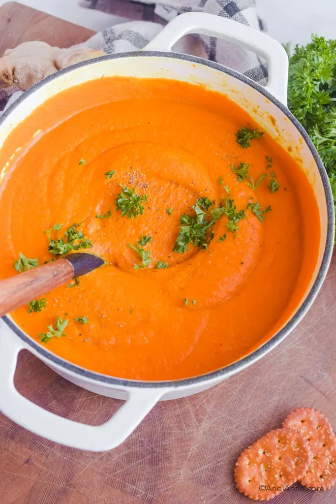 Looking down at pureed turmeric ginger carrot soup in a white pot with parsley sprinkled on top. 