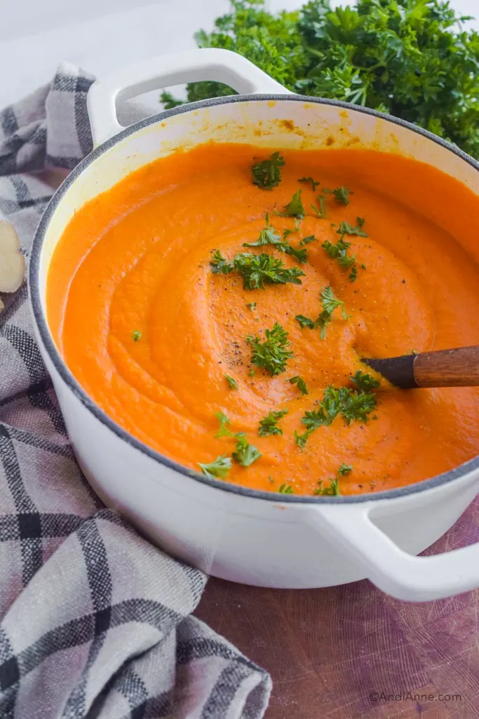 turmeric ginger carrot soup in a white pot with a bit of parsley and pepper sprinkled on top. 