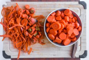 chopped carrots in a bowl with carrot skin scraps beside it and a knife.