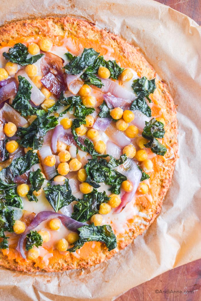 overhead view of cooked cauliflower pizza with kale, chickpeas, onion, sweet potato puree and mozzarella cheese.