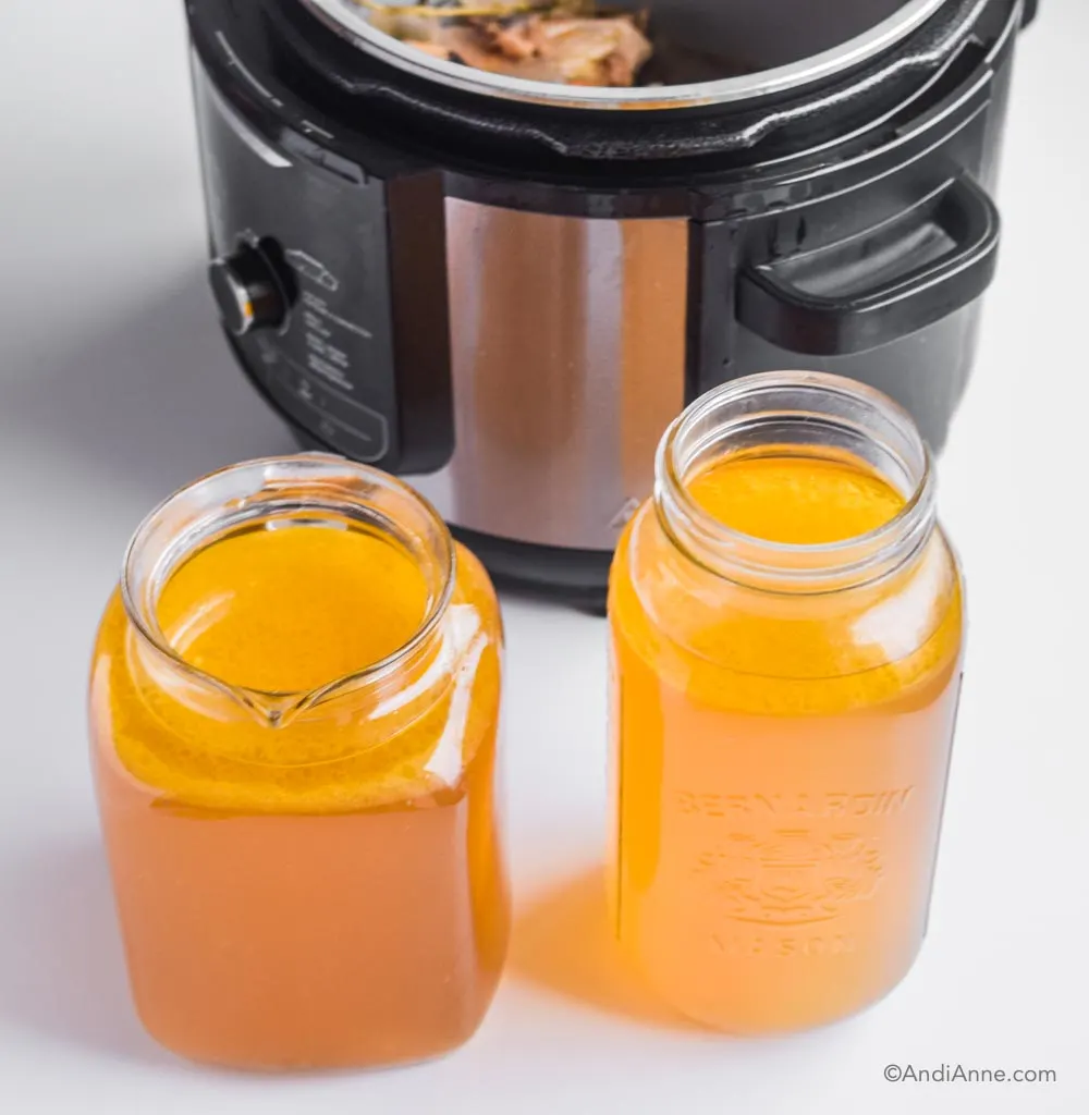 Two jars of hot bone broth placed in front of an instant pot.