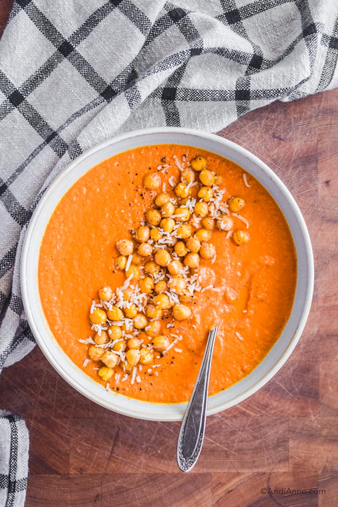 Looking down on carrot tomato soup. Roasted chickpeas and grated parmesan cheese are sprinkled in the center of the soup.