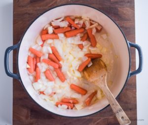 baby carrots and cooked onions in dutch oven pot with wooden spoon
