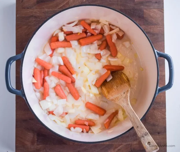 baby carrots and cooked onions in dutch oven pot with wooden spoon
