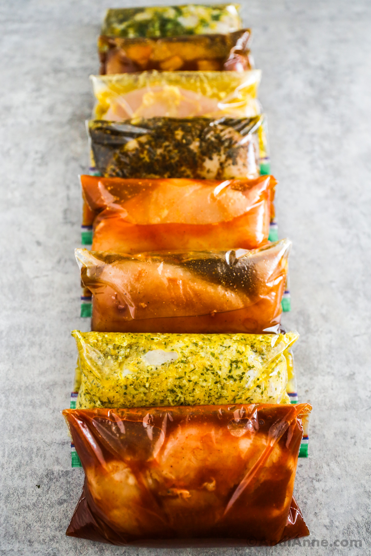 Various chicken marinades with raw chicken breast inside each bag all stacked beside each other on the counter.