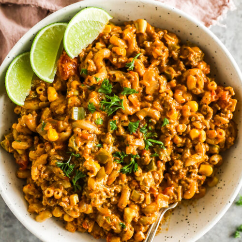 Taco pasta recipe in a white bowl with lime wedges.