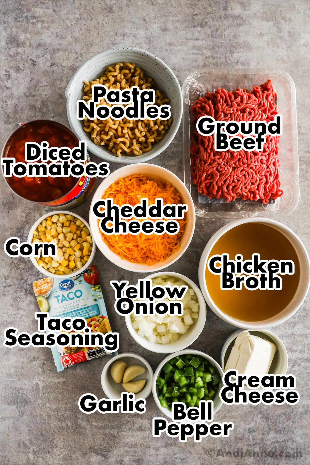 Recipe ingredients on the counter including raw ground beef, bowls of pasta noodles, diced tomatoes, cheese, corn, broth, onion, taco seasoning, cream cheese, and chopped bell pepper.