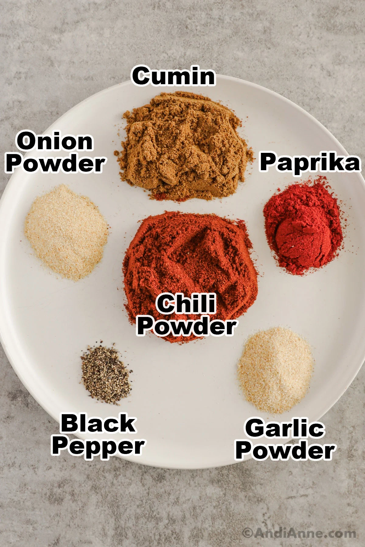 A plate with different spices in piles including cumin, paprika, onion powder, chili powder, black pepper, and garlic powder.