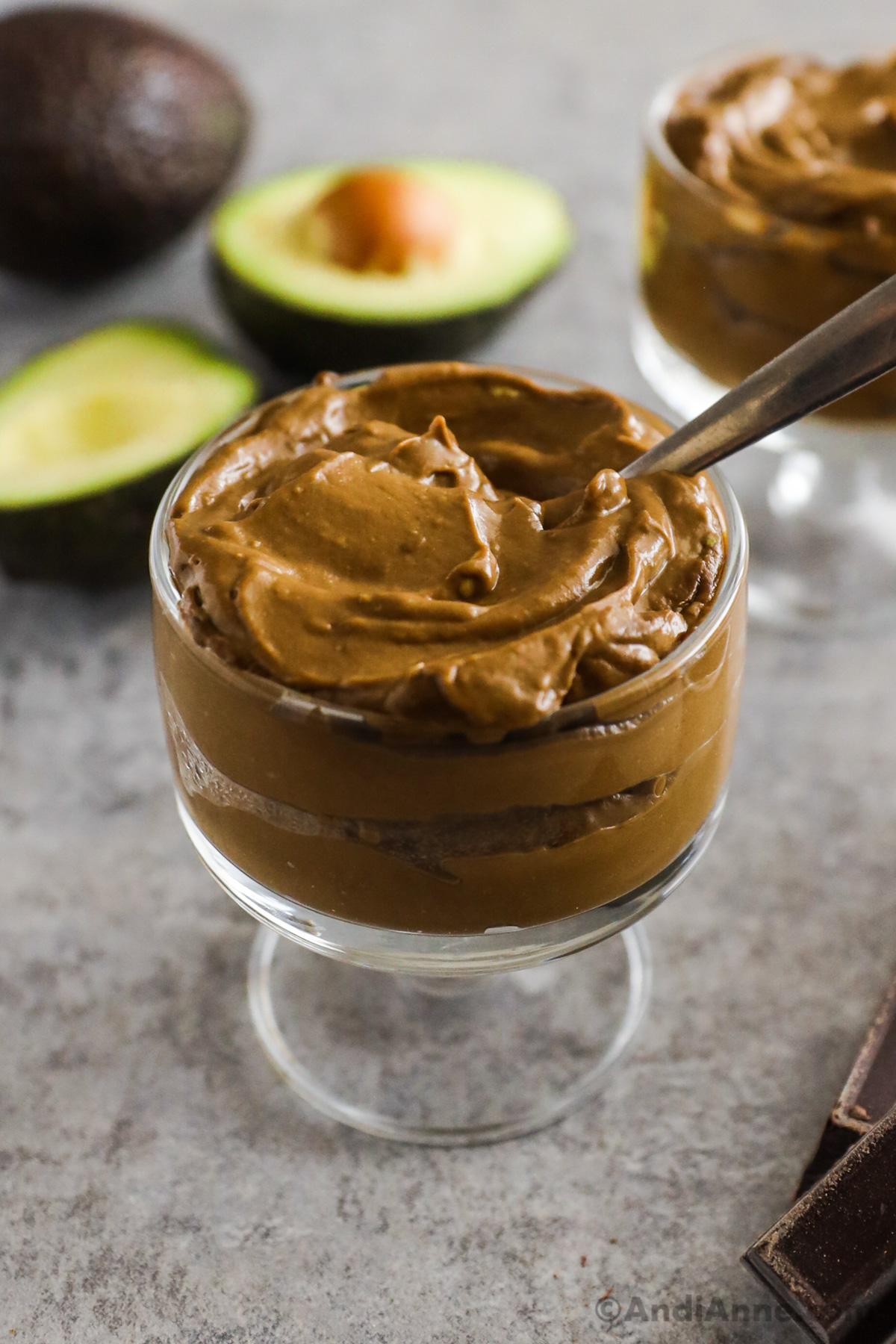 A glass dish with chocolate pudding and sliced avocado in the background.