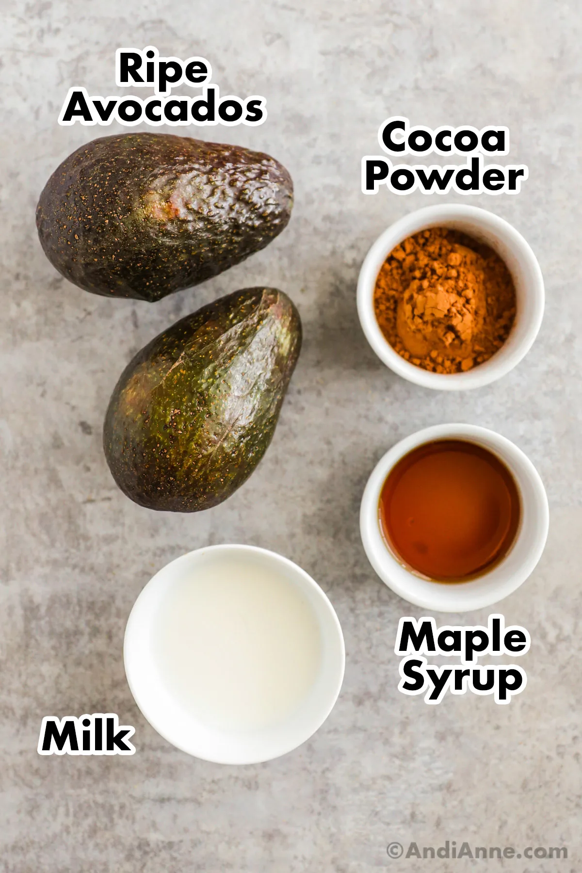 Recipe ingredients on the counter including two ripe avocados, cocoa powder, maple syrup, and milk.