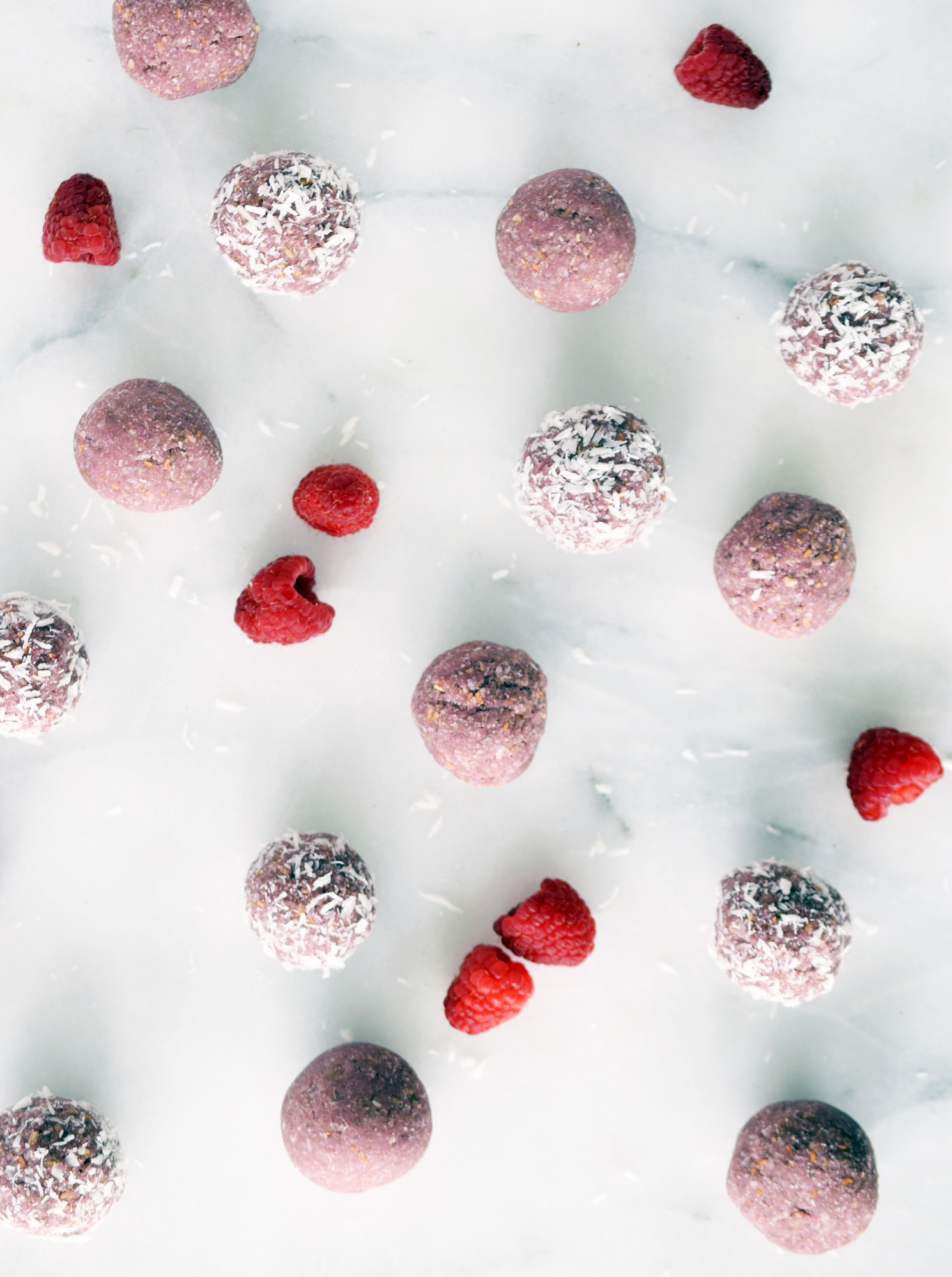 raspberry coconut energy balls on a marble counter with fresh raspberries around them
