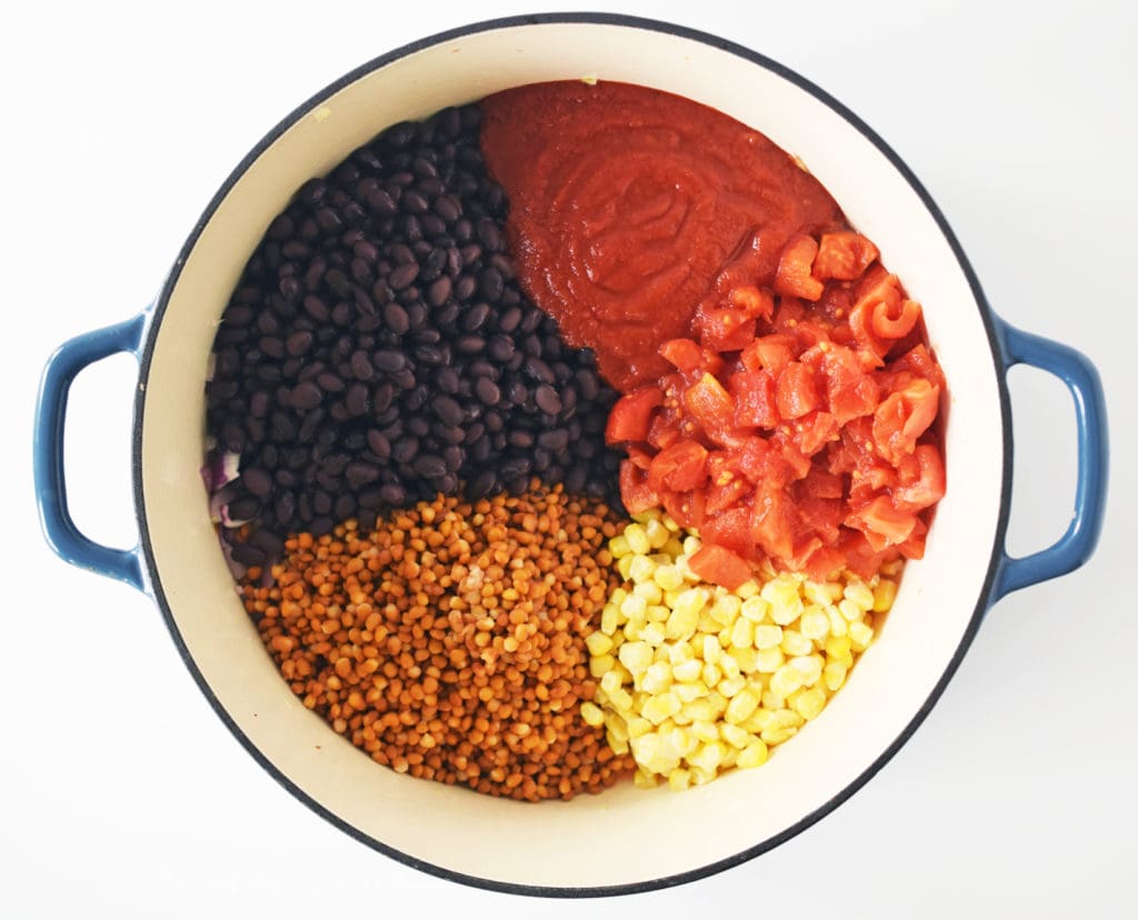 ingredients divided separately in a large blue pot, including black beans, lentils, frozen corn, crushed tomatoes, and diced tomatoes