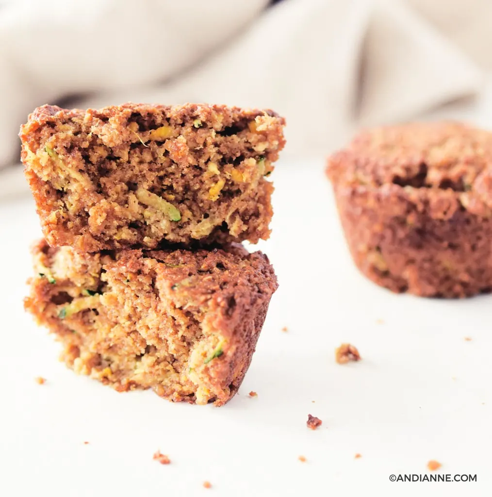 zucchini orange oat muffins stacked on top of eachother. Beige napkin in background. 