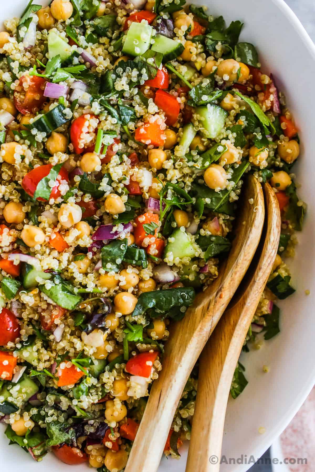 Close up of quinoa salad recipe with chickpeas, cucumbers and carrots and wood serving spoons.