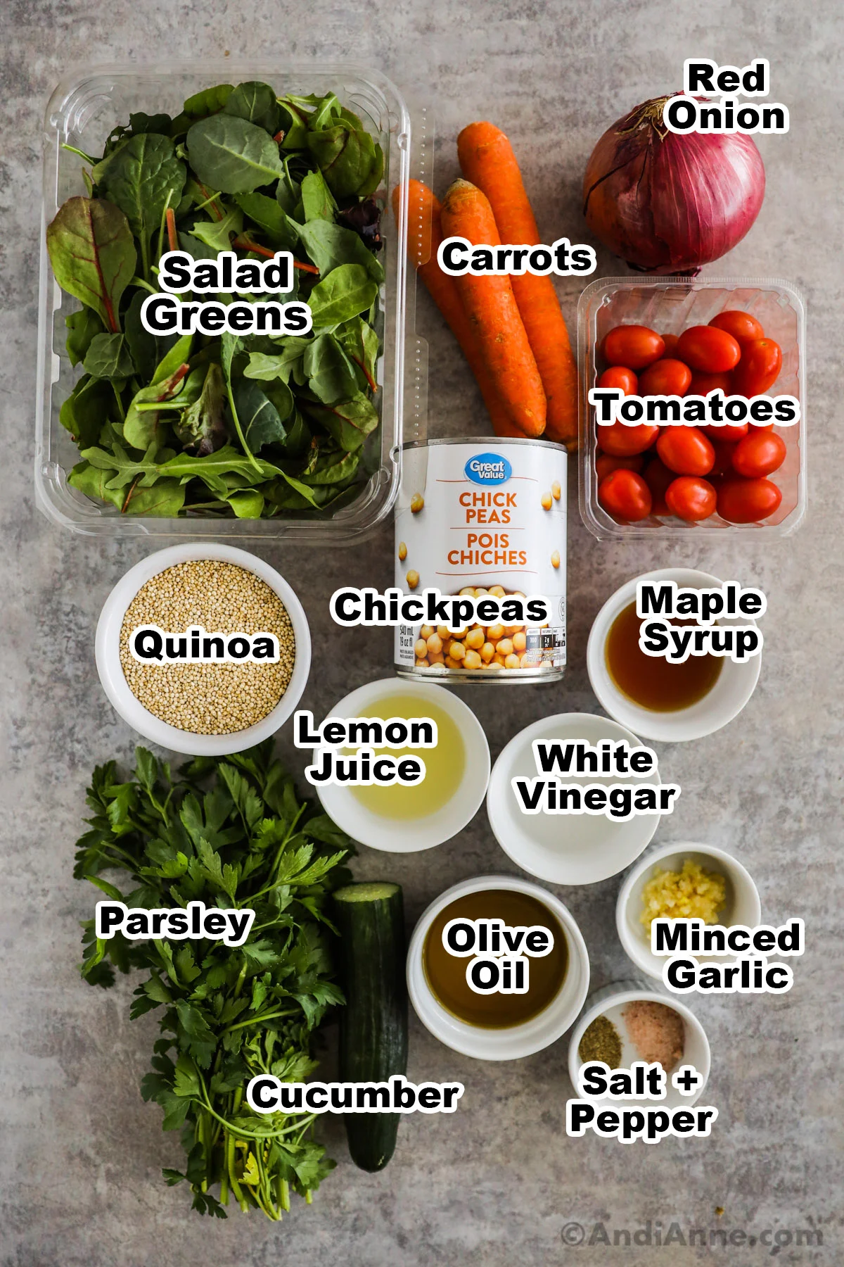 Recipe ingredients including containers of salad greens, tomatoes, can of chickpeas, bowls of quinoa, lemon juice, vinegar, olive oil, maple syrup, half a cucumber and a bunch of parsley.