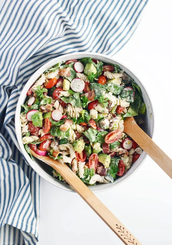 blt pasta salad with wood spoons in a white bowl and striped napkin