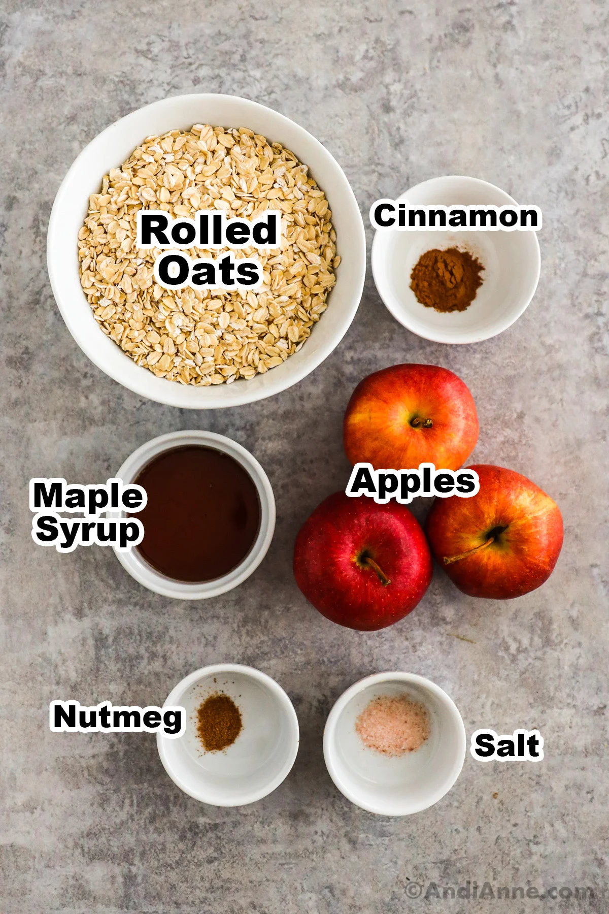 Recipe ingredients on the counter including rolled oats, cinnamon, maple syrup, nutmeg, salt and fresh apples.