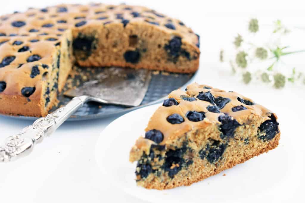 Gluten free blueberry cake sliced and on a white plate with silver pie cutter