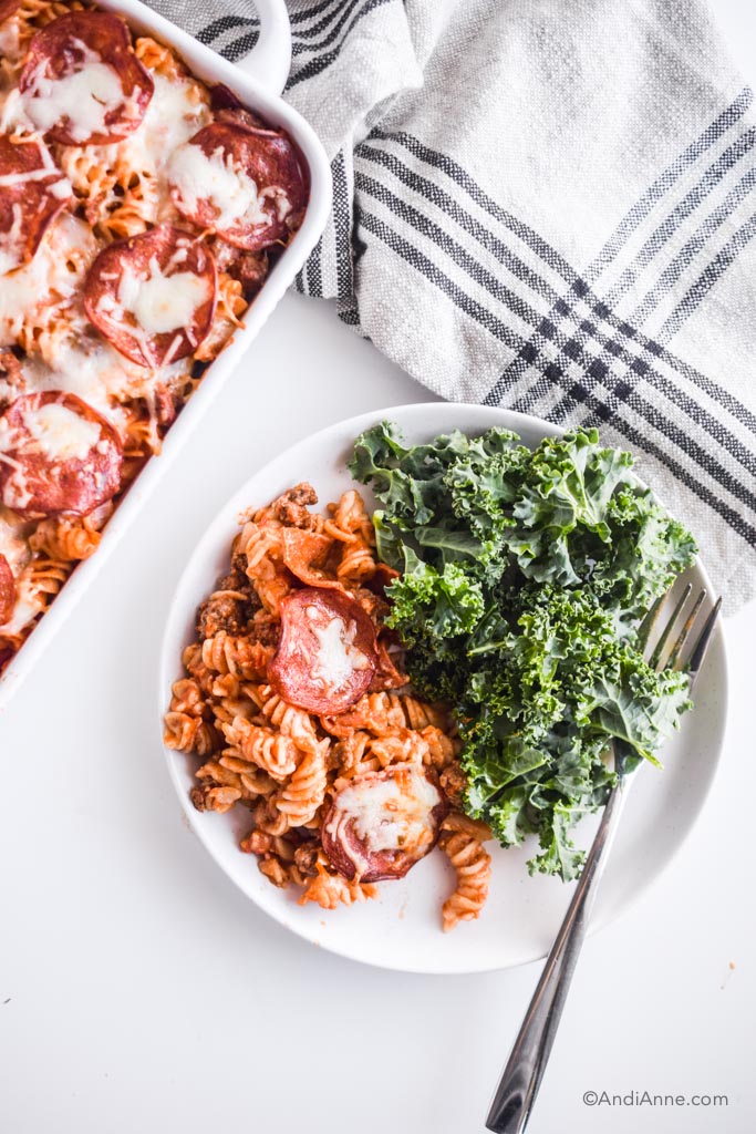 pizza pasta bake on a white plate with kale salad and a fork