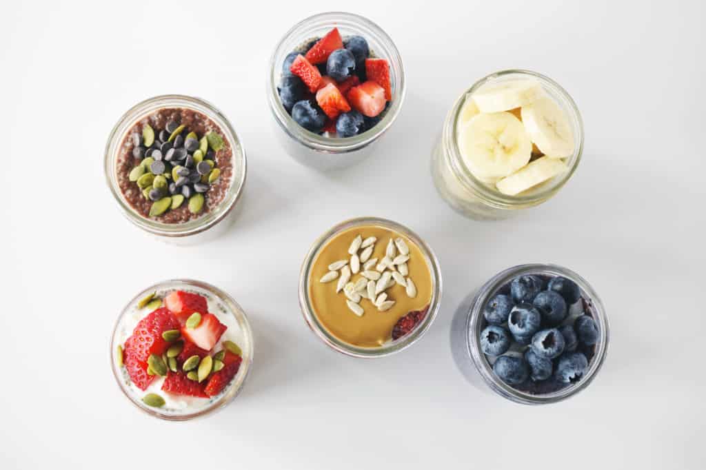 birds eye view of tops of mason jars with fresh berries, banana slices, seeds and chocolate chips sprinkle in each