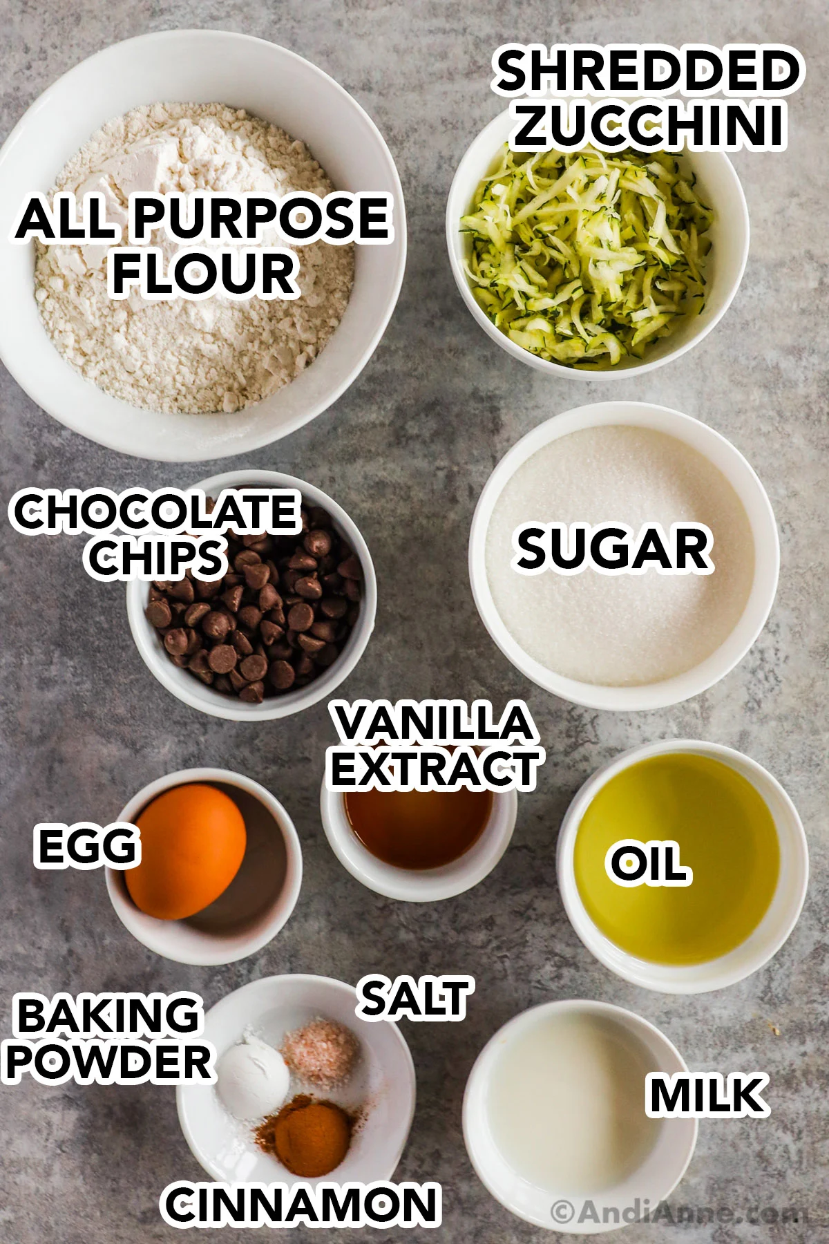 Recipe ingredients in bowls on the counter including flour, shredded zucchini, chocolate chips, sugar, vanilla extract, oil, egg, milk, and cinnamon.