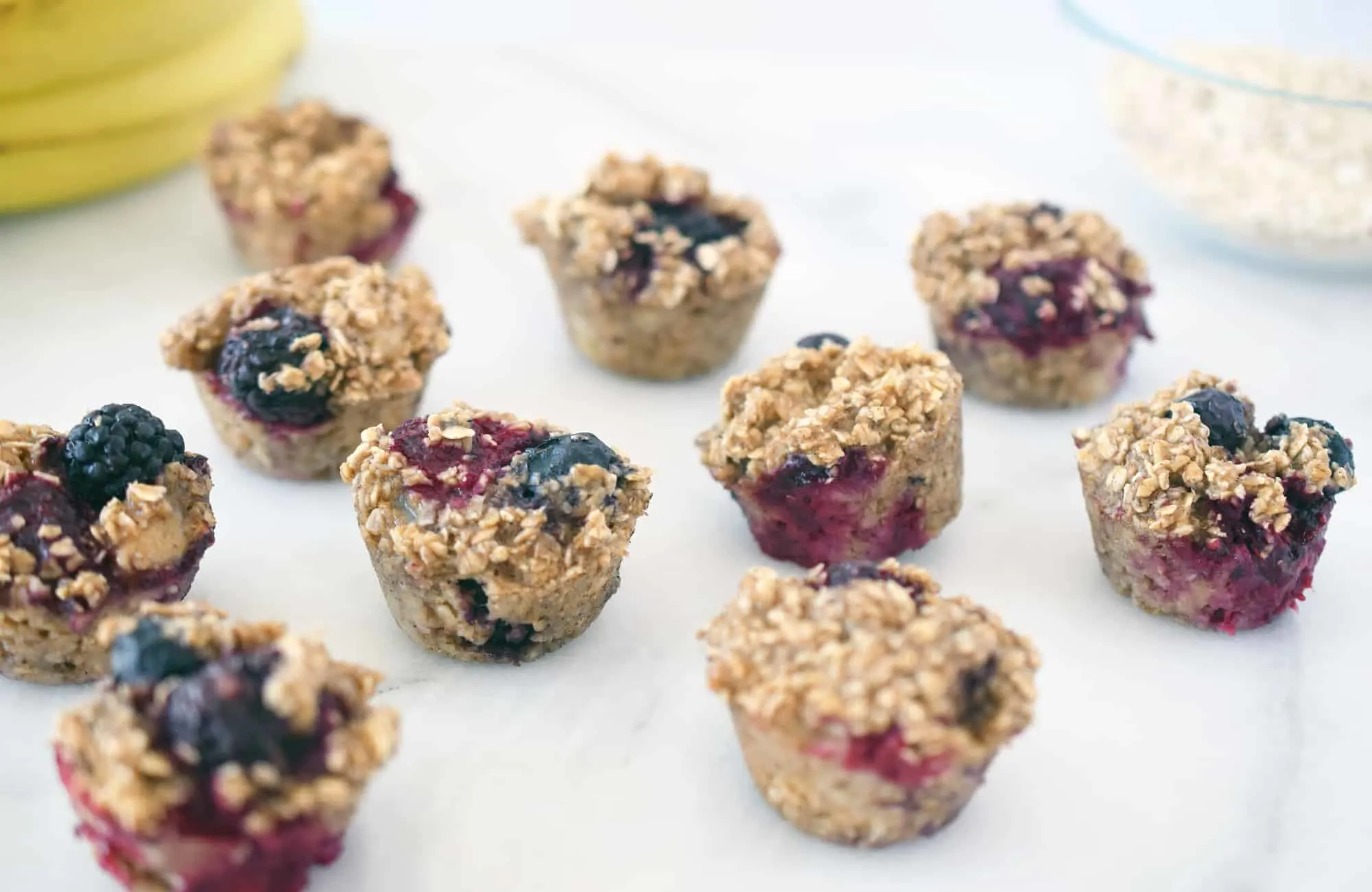 oat berry mini muffins on a white counter with bananas and bowl of rolled oats in the background