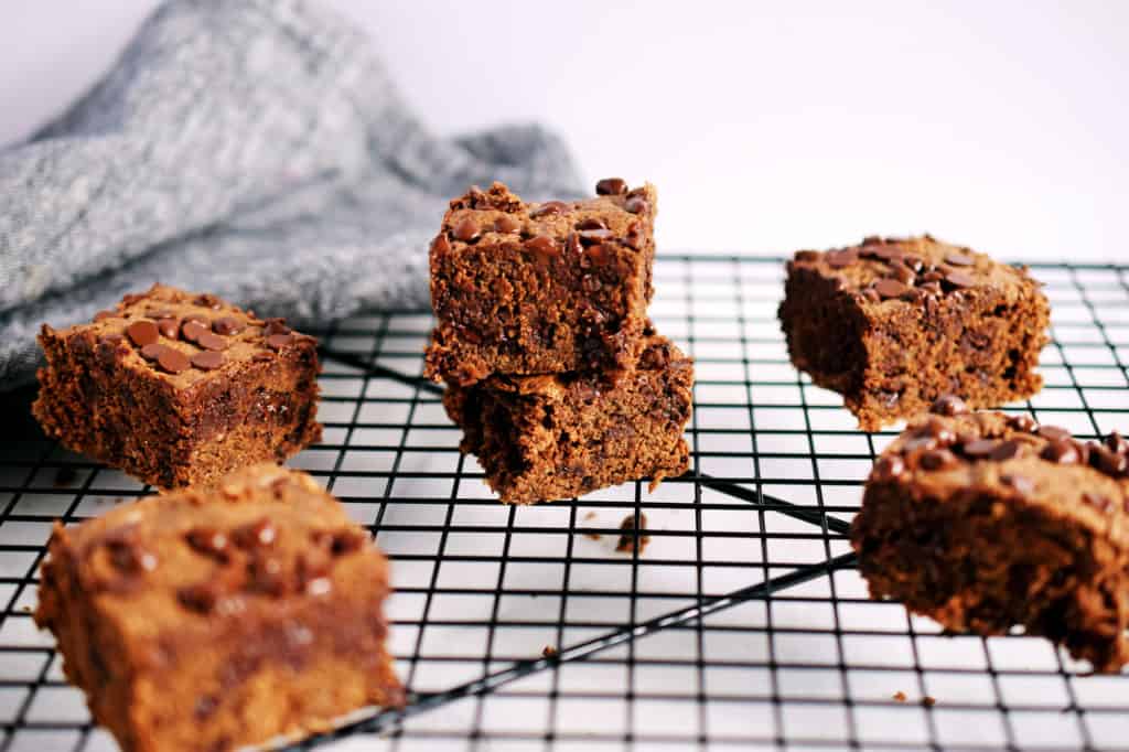 nut butter oat brownies in squares stacked on a black cookie rack with grey napkin in background