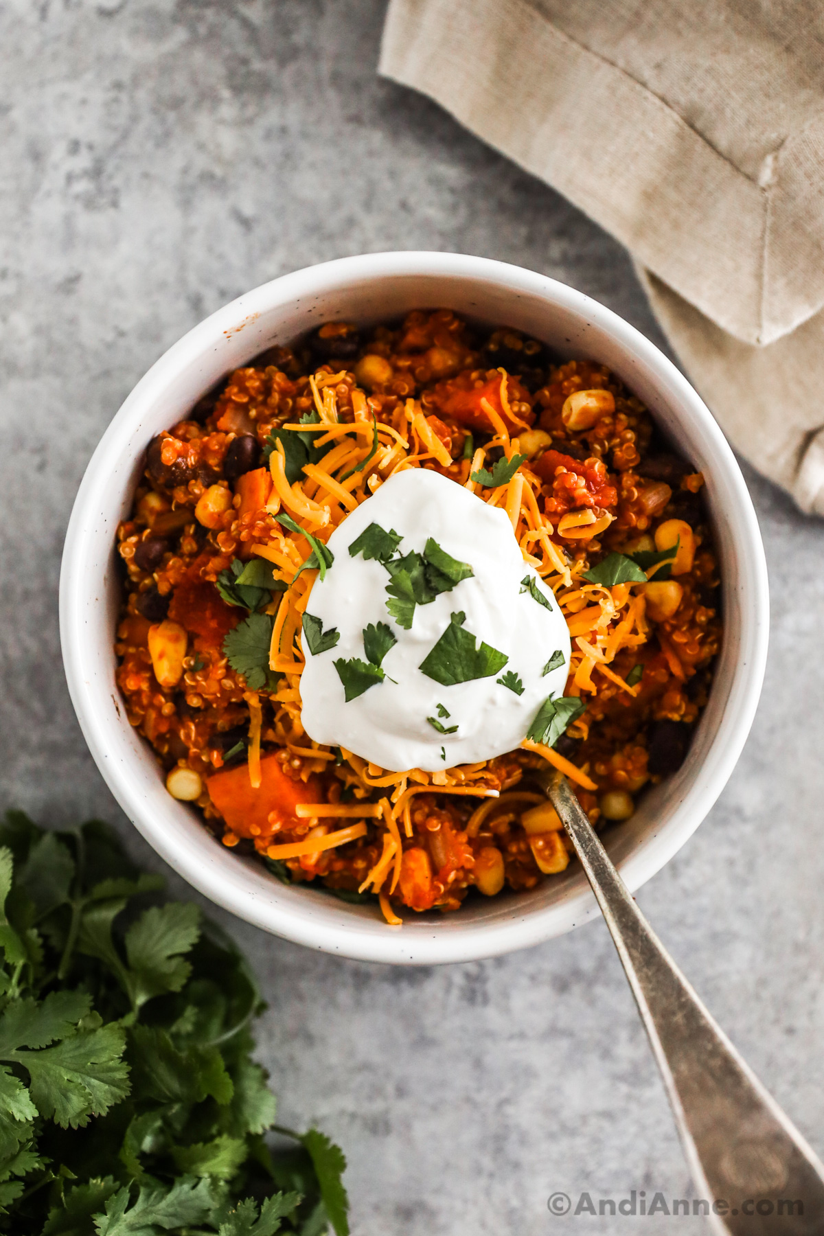 A bowl with quinoa chili topped with shredded cheese, a dollop of sour cream and chopped parsley.