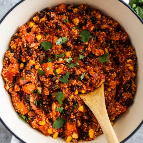 A large white pot with sweet potato quinoa chili inside and a wood spoon.