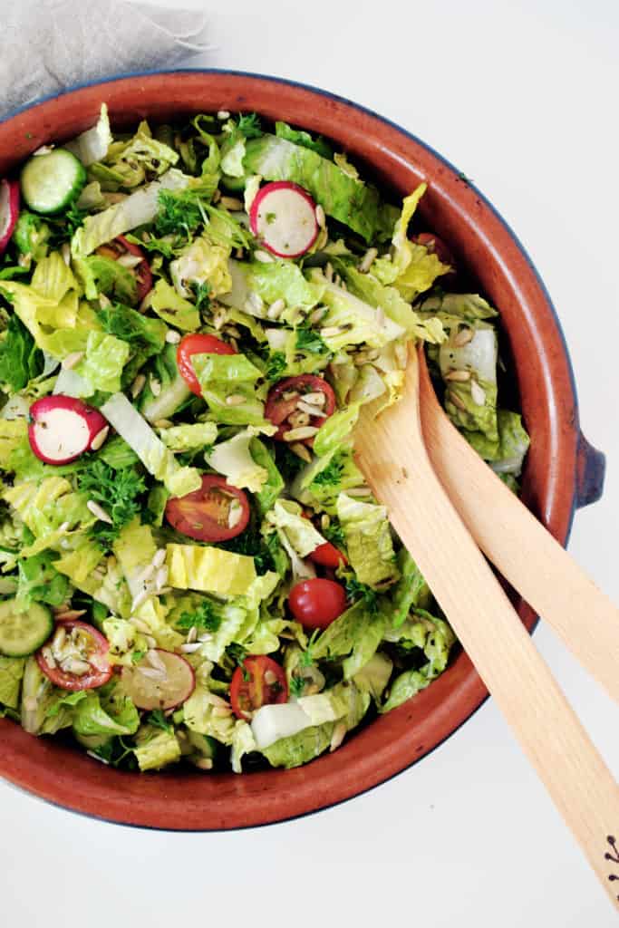 garden salad with herb dressing in brown bowl with wooden salad spoons