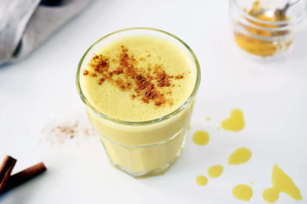 turmeric ginger latte in glass with cinnamon sprinkled on top. napkin and small mason jar in background