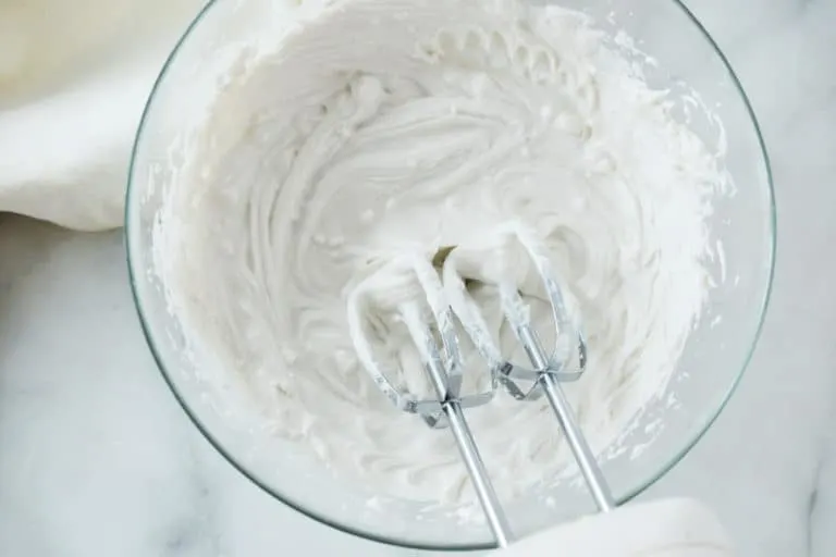 glass bowl with coconut cream inside and hand mixer in bottom right