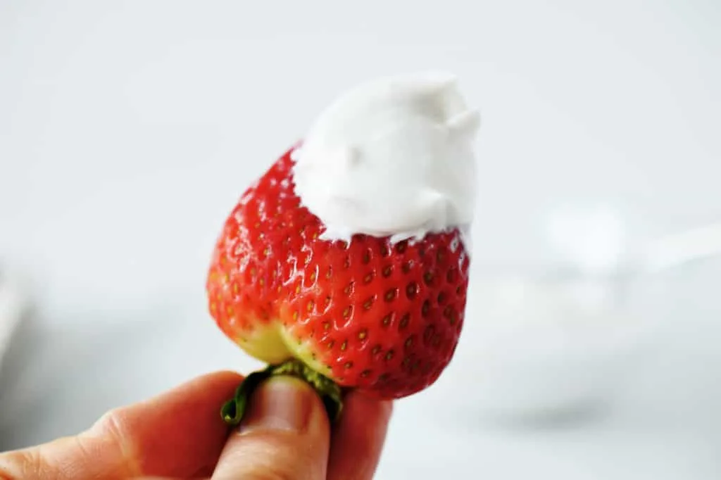 hand holding strawberry with dollop of whipped coconut cream on top