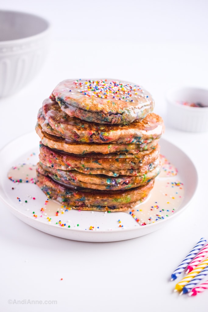 Birthday sprinkle pancakes on a white plate with candles in foreground