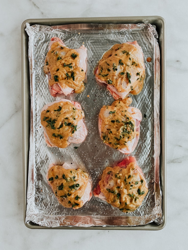 raw chicken with sauce poured over top on a baking sheet
