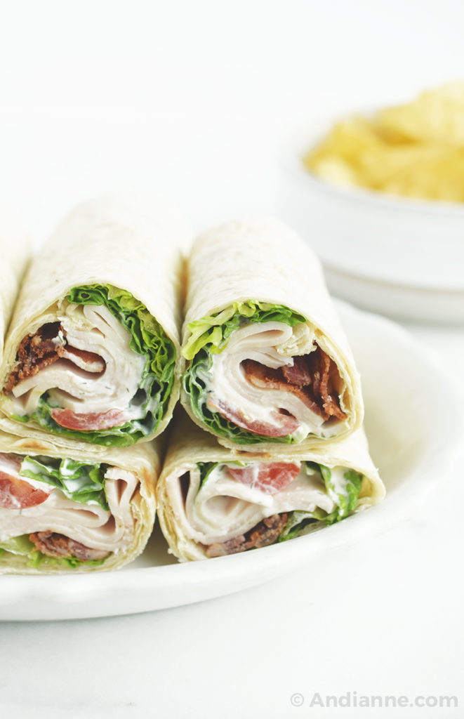 chicken bacon ranch wraps rolled and stacked on a plate with tortilla chips in background