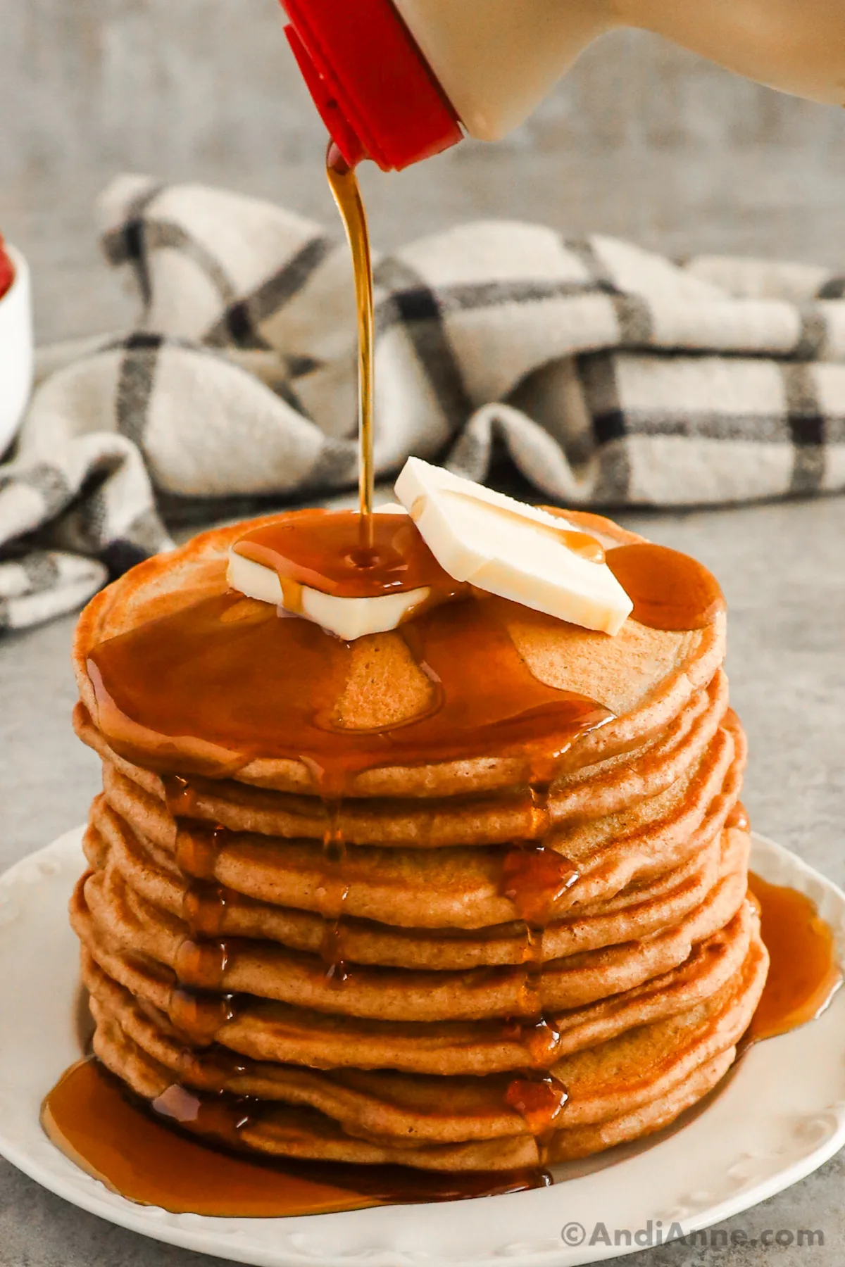 Close up of a stack of pancakes drizzled with maple syrup and topped with butter.