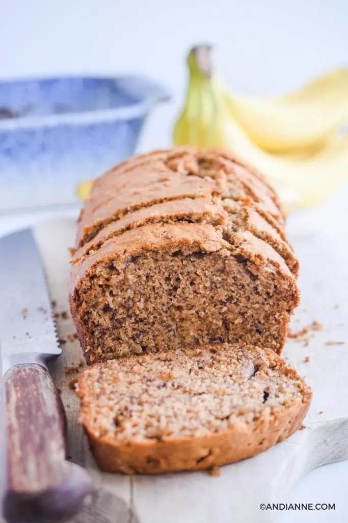 sliced banana bread with bread knife and bananas in background