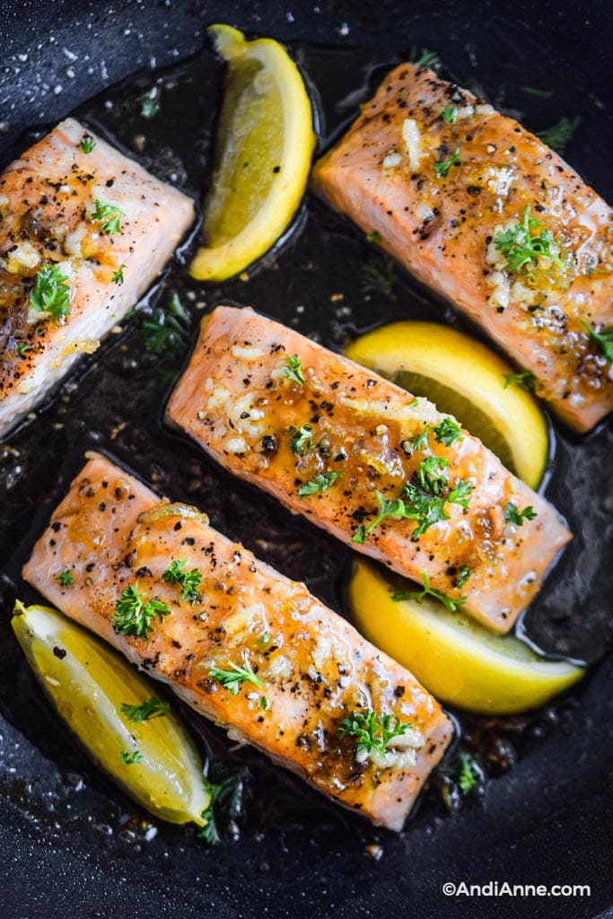 close up of honey garlic salmon fillets in a frying pan with lemon slices