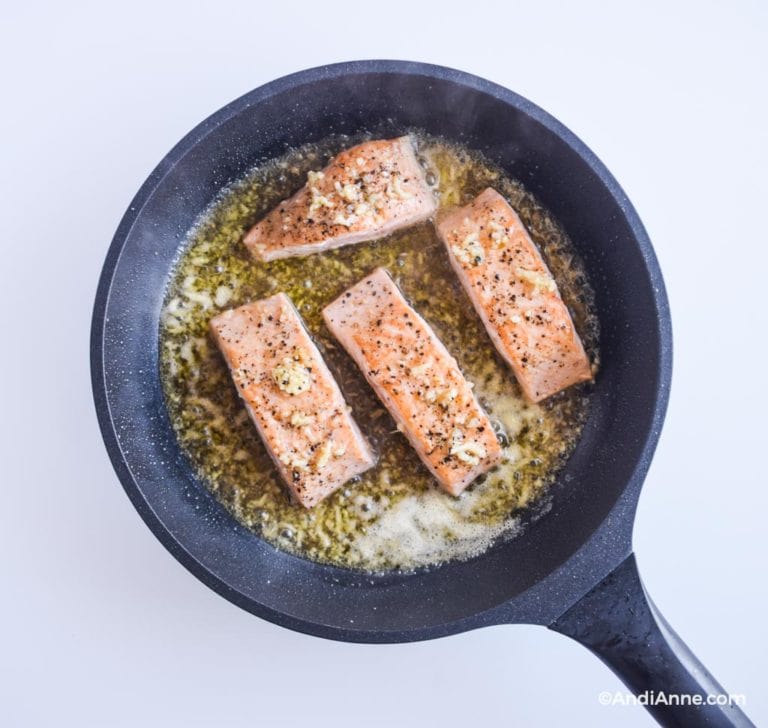 cooking salmon fillets in frying pan with honey glaze sauce surrounding