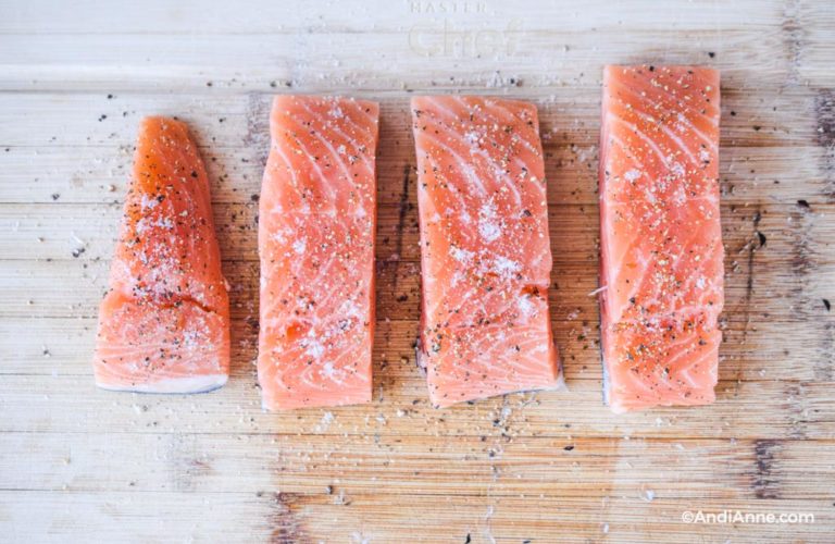 four raw salmon fillets on a cutting board seasoned with salt and pepepr