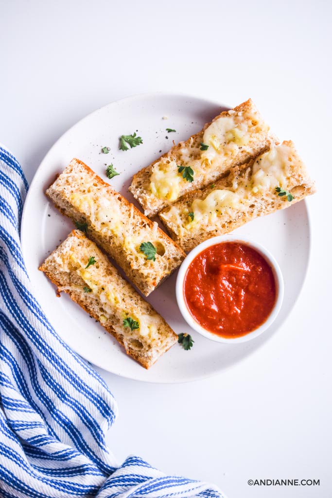cheesy garlic french bread sticks on a white plate with a small bowl of pizza sauce