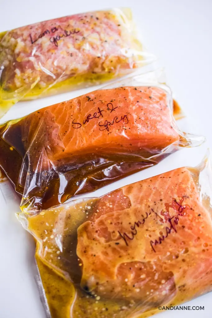 three pieces of salmon marinating inside plastic bags with handwriting on top of each