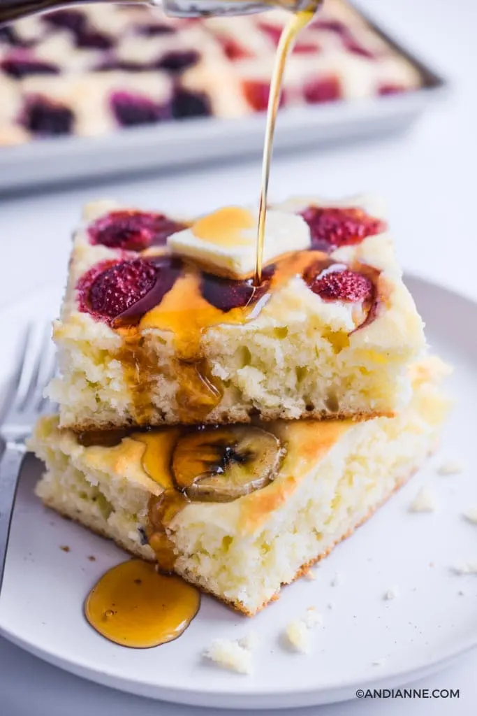 sheet pan pancakes stacked on top of eachother on a white plate. Butter on top and drizzled with maple syrup.