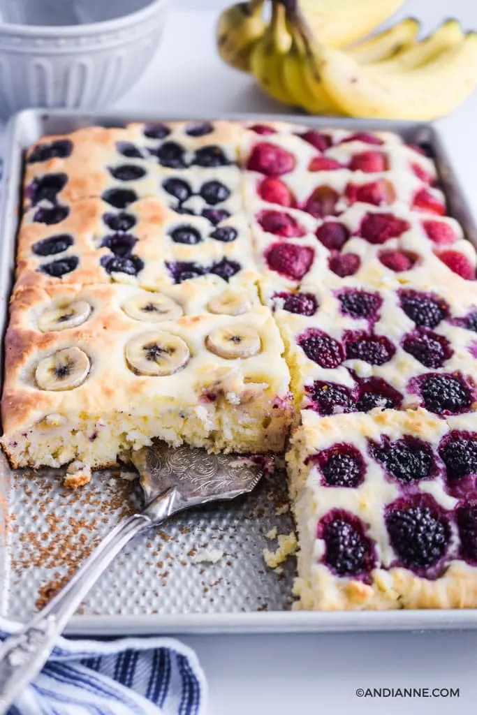 close up of sheet pan pancakes in a pan with spatula. Bananas and grey bowl in background.