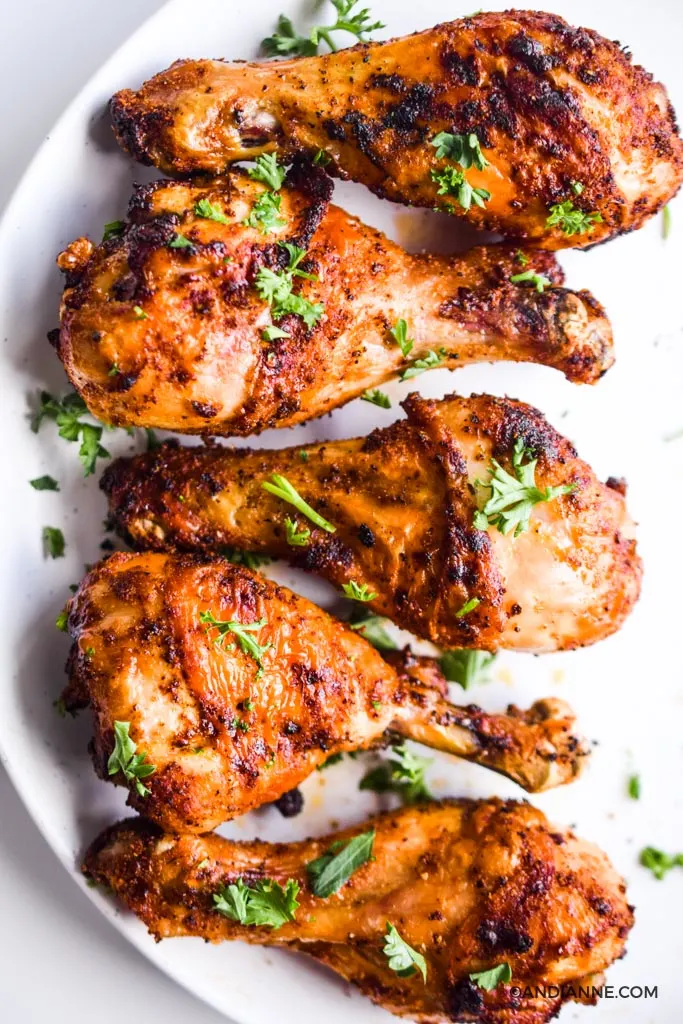 five cooked air fryer chicken drumsticks on a white plate sprinkled with bits of parsley