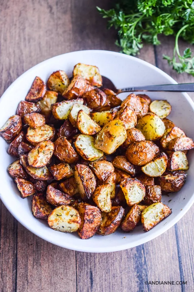 air fryer potatoes in a white bowl with spoon and parsley on the side.