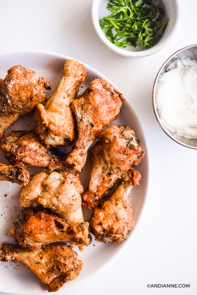 air fryer salt and pepper wings on white bowl with smaller white bowl of parsley and silver bowl of ranch dip in top right corner